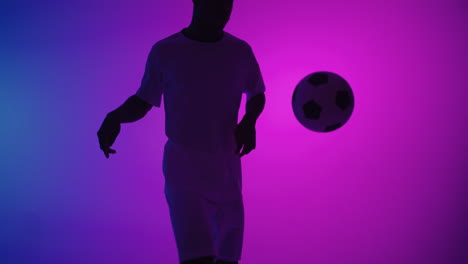 hombre negro un jugador hace malabares con una pelota de fútbol en un estudio oscuro con luces de neón en el suelo y efectos de iluminación roja y azul en cámara lenta. jugador de fútbol profesional africano