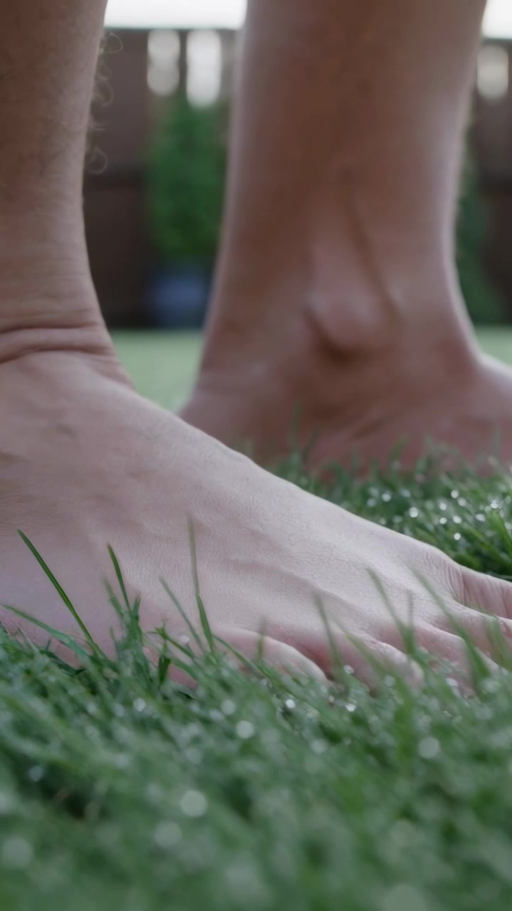 Vertical video: Placing front foot, bare feet and ankles pressing into dewy lawn, preparing to step