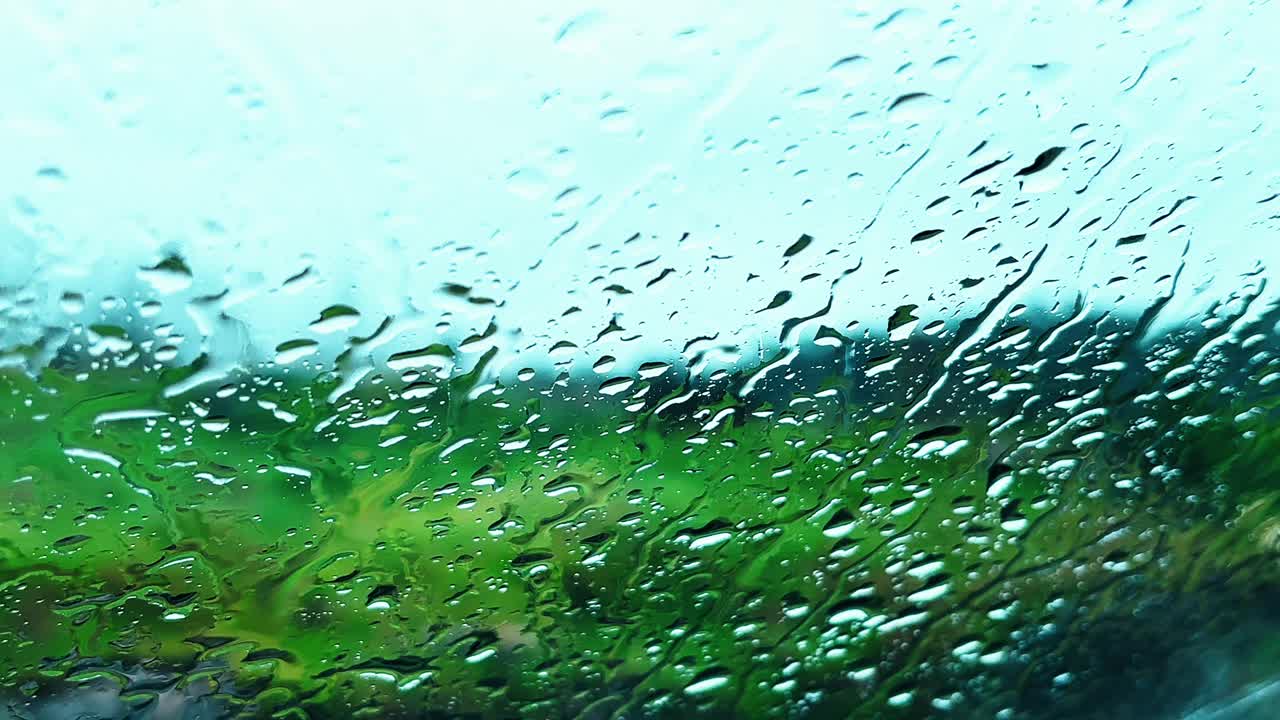 Rain on glass blurs lush countryside view under soft daylight