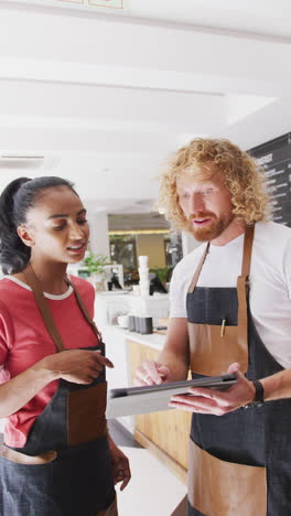 vertical video of happy diverse male and female baristas using tablet in cafe