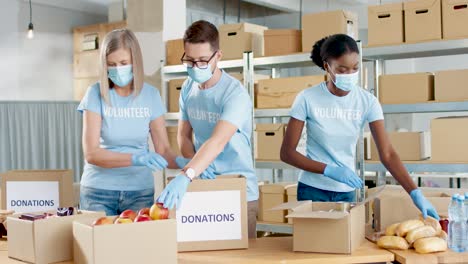grupo multiétnico de voluntarios en cajas de embalaje de máscaras faciales con comida y agua en un almacén de caridad