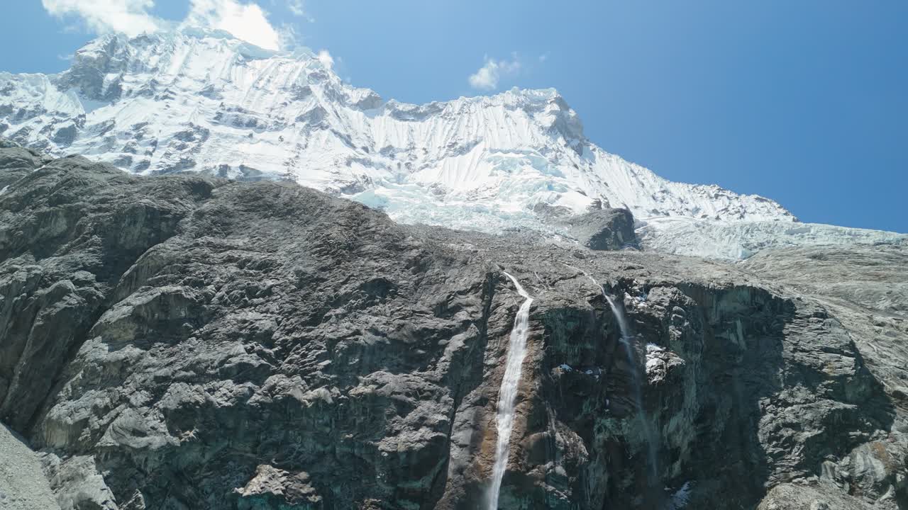 A slow tilt-up reveals glacial waterfalls cascading from snowy Chacraraju Mountain into the vibrant turquoise waters of Laguna 69 in Peru’s Cordillera Blanca