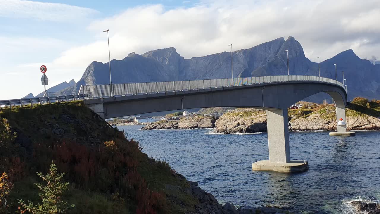 Bro över fjorden i Hamnoy med ett imponerande, kargt berglandskap i bakgrunden.