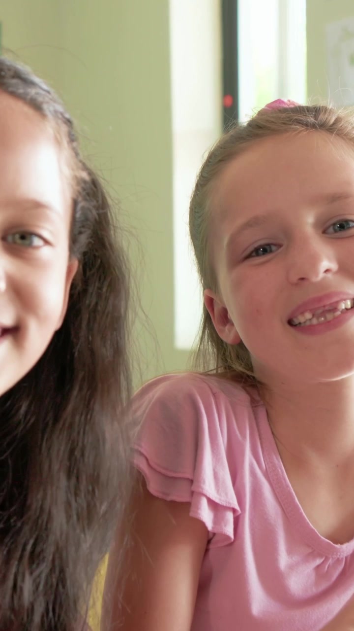 Video verticale: Ragazza in magenta che si avvicina a una ragazza in rosa, toccando il tablet in classe, sorridendo.
