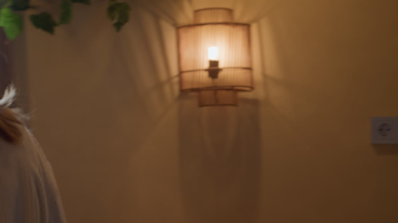 Woman wearing glasses holds notebook while opening glass door, walking toward table with cup already placed, indoor setting with large windows and soft natural daylight illuminating modern background