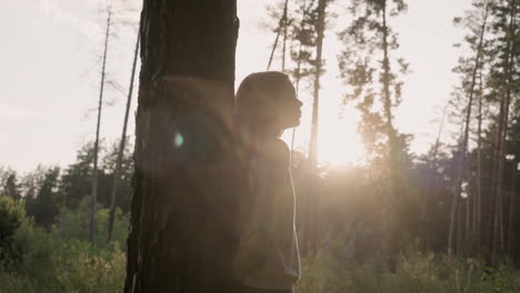 a young woman stands in front of a tree in a forest at sunset