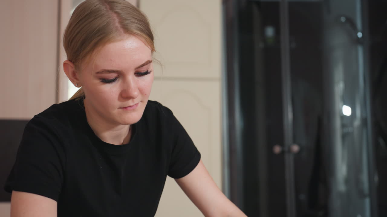 Dedicated massage therapist wearing black deeply focused during treatment session, hands extended forward while standing beside blurred wardrobe in softly lit spa interior with calm neutral tones