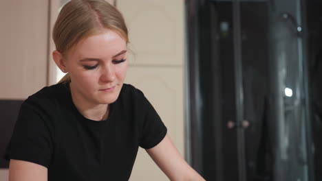 dedicated massage therapist wearing black deeply focused during treatment session, hands extended forward while standing beside blurred wardrobe in softly lit spa interior with calm neutral tones