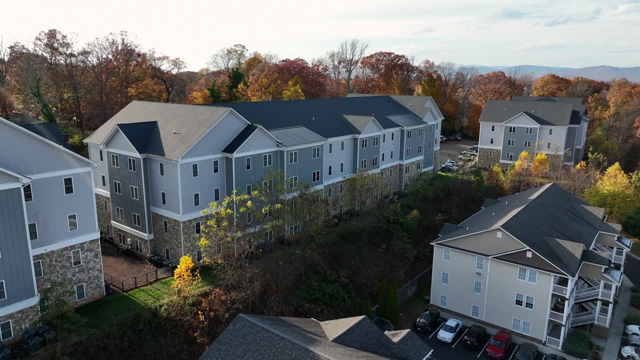 Sweeping aerial drone footage showcases a tranquil USA suburb at peak autumn. Rows of houses nestle among colorful trees bathed in golden light evoking warm seasonal beauty