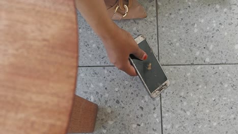 picking up a broken smartphone with a cracked screen