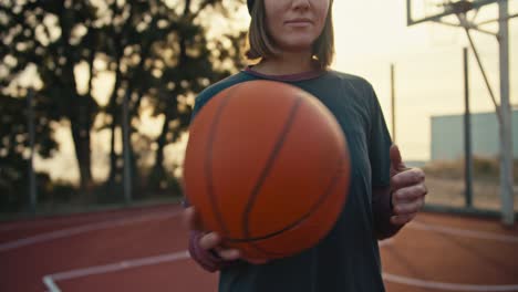 Close-up-portrait-of-a-blonde-girl-with-a-bob-hairstyle-in-a-sports-uniform-throws-an-orange-basketball-from-hand-to-hand-during-morning-basketball-training-on-a-street-court