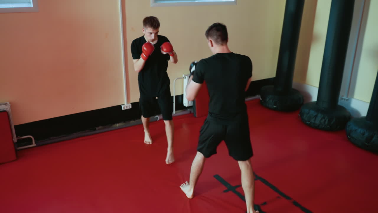 Wrestlers engaged in boxing sparring session inside gym, one man in red gloves defending while opponent in black gloves prepares punch, showcasing combat skills, intensity, focus, discipline