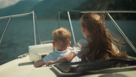 smiling little children lean out of cabin exit riding motorboat in scenic sea. cheerful brother and sister sail modern yacht in ocean on summer holiday