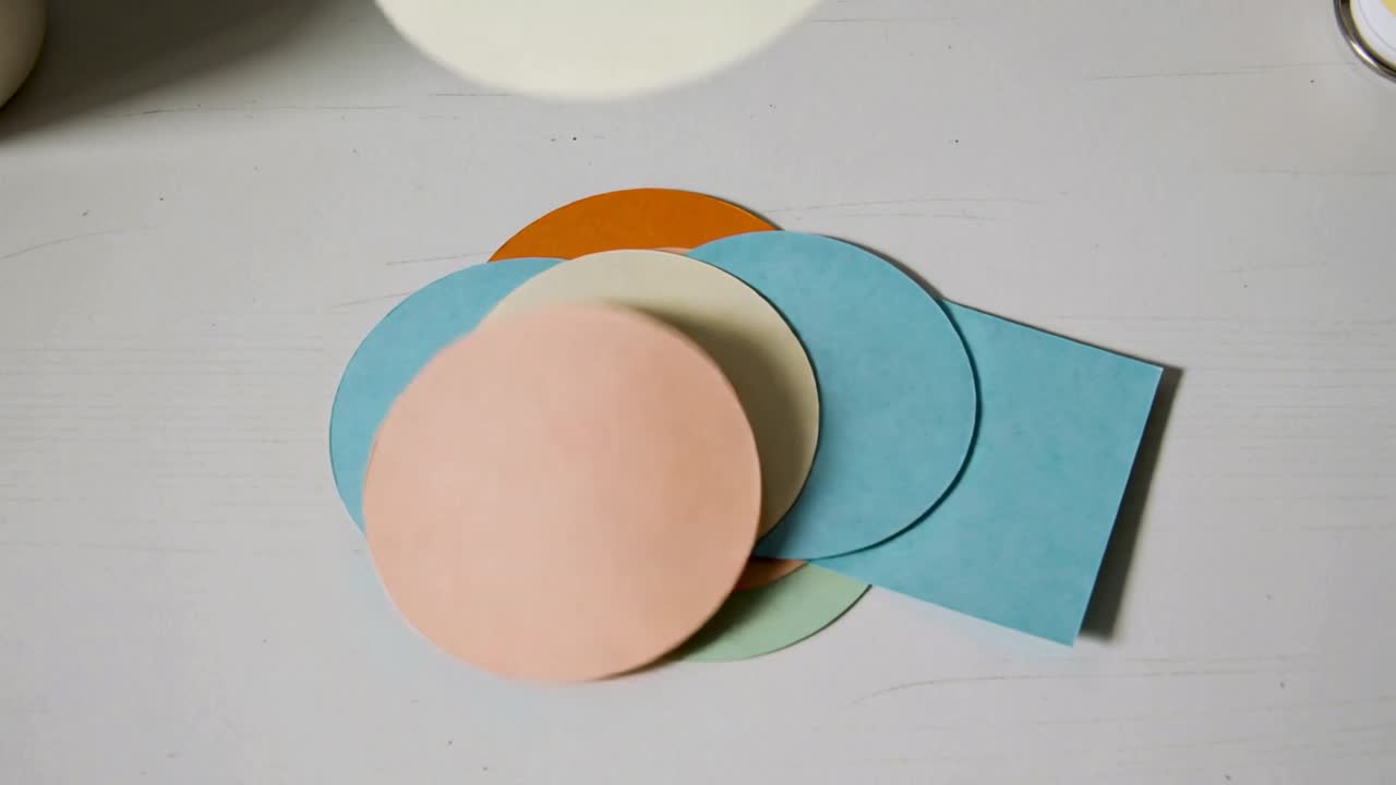 Pastellfarbene Papierschnitte fallen von oben herab, stapeln sich auf einer blauen Karte und formen ein mehrschichtiges Kunstwerk.