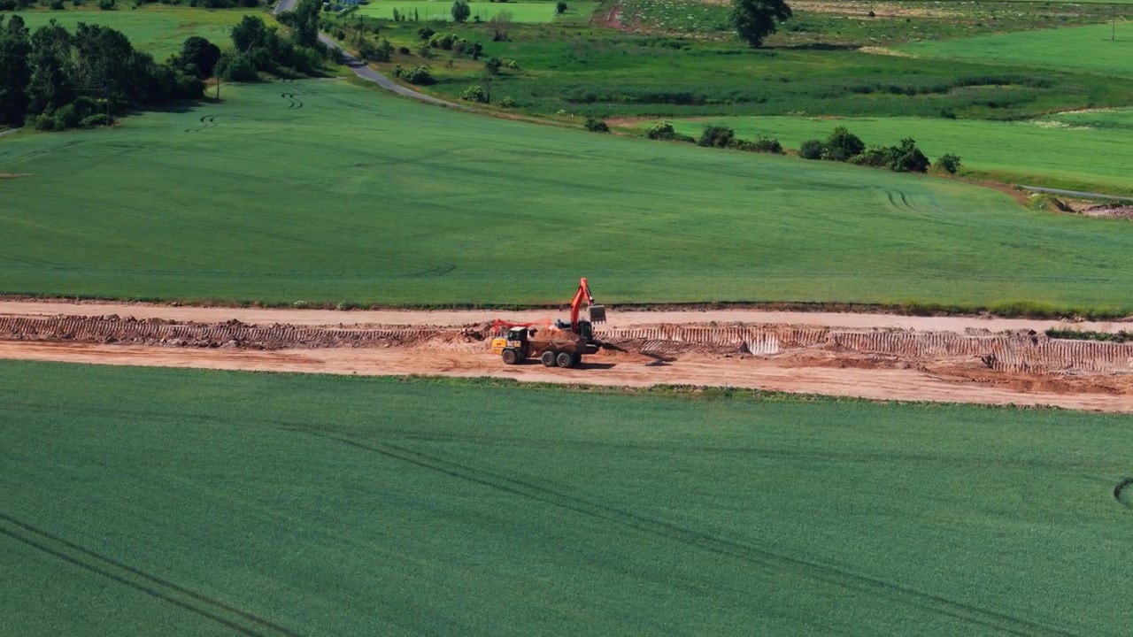 Ripresa dall'alto di macchinari pesanti al lavoro in un cantiere per la costruzione di una nuova tangenziale, circondato da campi verdi. Utile per lo sviluppo di infrastrutture e progetti di ingegneria civile.