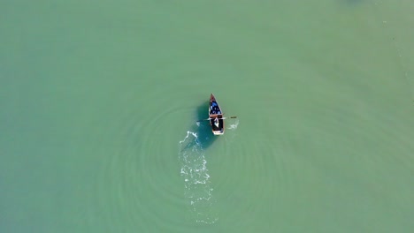 isolated and unrecognizable fisherman rowing on small boat in calm sea or river waters, dominican republic