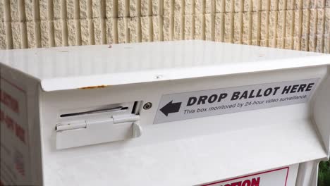 young minority black man votes by dropping mail-in ballot letter in slot at official voting box with drop ballot here sign