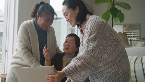 Happy-senior-asian-mother,-adult-daughter-and-granddaughter-sitting-in-living-room-using-laptop