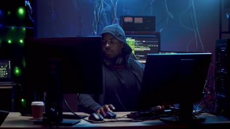 young man hacker commiting cybercrime while hacking at two computers in the dark programming room with technologies 1