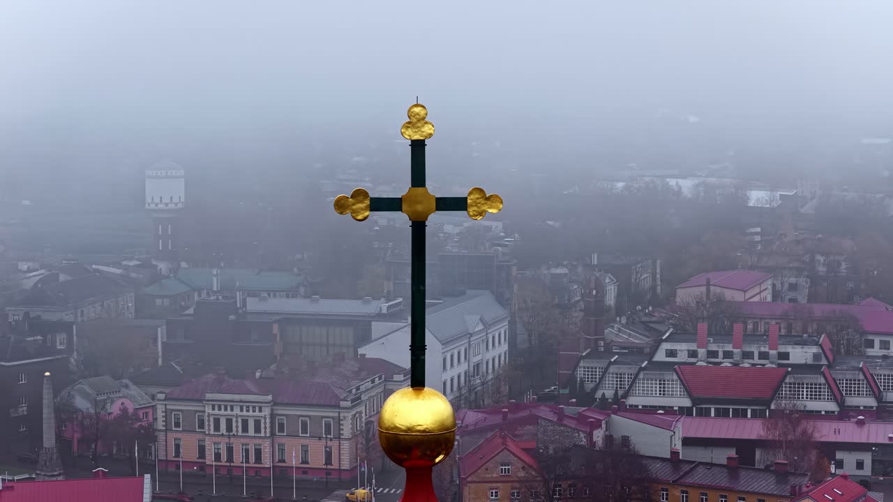 Foggy Cēsis cityscape with church cross in Latvia, misty and serene mood