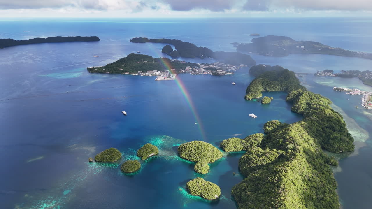 Cinematic drone shot circling and revealing the pristine turquoise sea and lush islets around Palau with a bright rainbow shining. Wide cinematic aerial shot