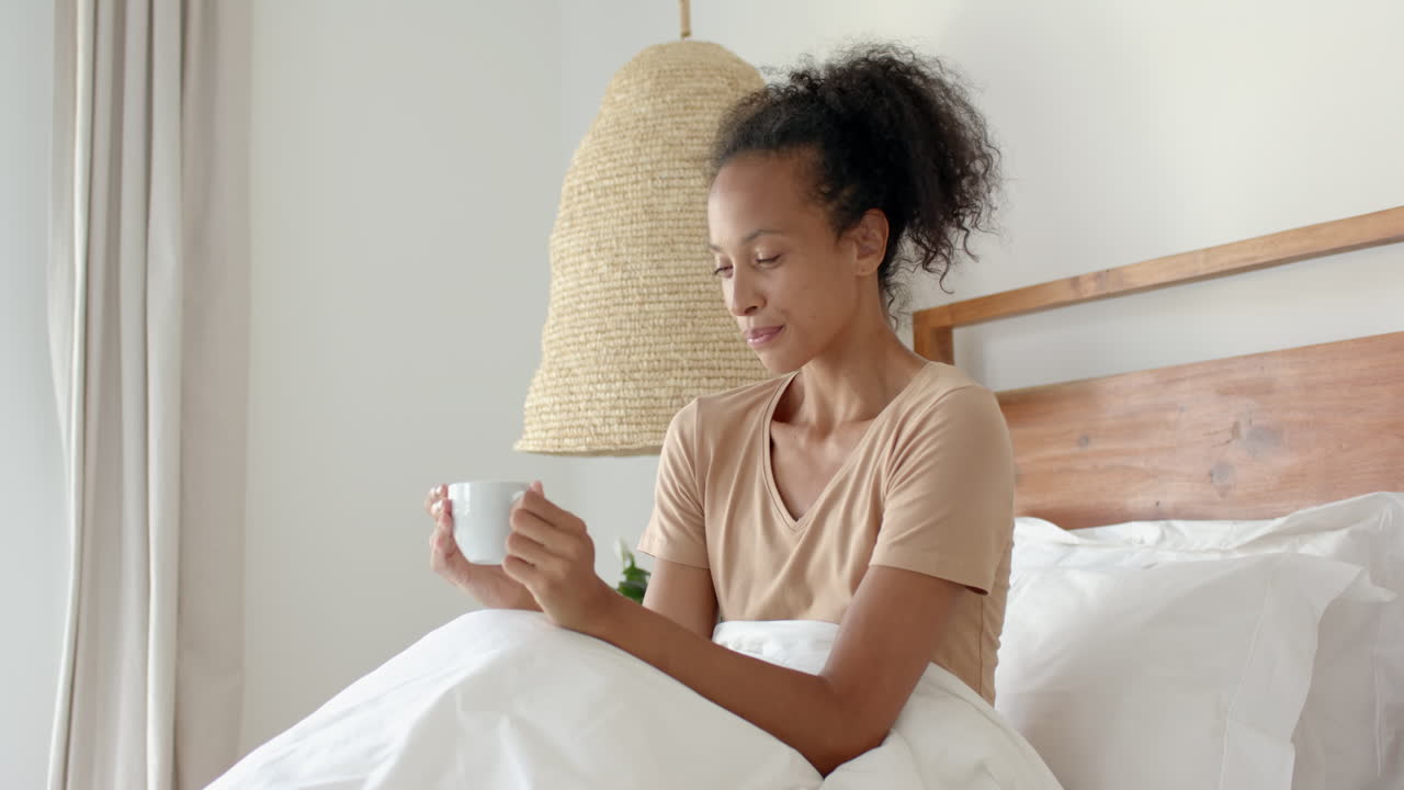 woman relaxing in bed, enjoying coffee and browsing smartphone, at home