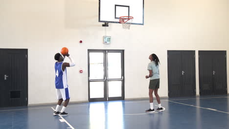 African american male basketball player bouncing with coach giving instructions in gym