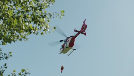 Medical-Air-Rescue-helicopter-flying-away---green-leaves-in-foreground---slowmotion