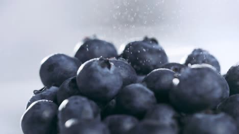 extreme close-up of water particles pouring on top of blueberries pile in slow motion