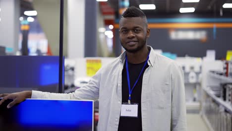 Smiling-salesman-showing-tv-stands-among-appliances-in-a-store,-Slow-Motion-video