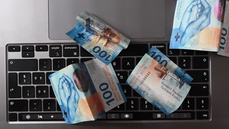 vista superior de billetes de banco de 100 dólares en un teclado portátil, ganancias obtenidas en internet con un negocio en línea, francos suizos