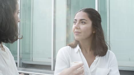 alegres amigas de la oficina sentadas afuera, bebiendo café, hablando y riendo