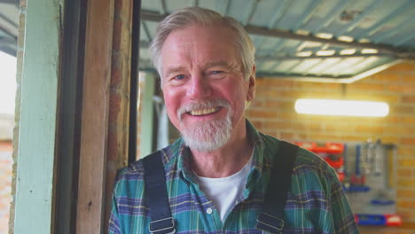 portrait of senior male wearing overalls in garage workshop