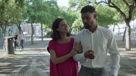 una pareja sonriente hablando mientras pasean por el parque de verano.