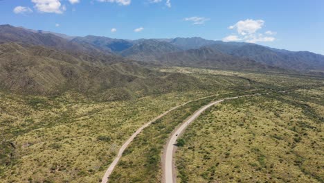 Two-vehicles-from-afar-traveling-lonely-road-through-Mendoza-arid-valley