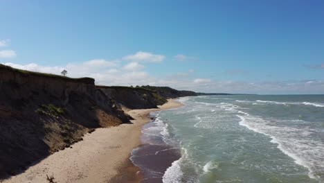 Flying-Over-Coastline-Baltic-Sea-Ulmale-Seashore-Bluffs-Near-Pavilosta,-Latvia-and-Landslides-With-an-Overgrown,-Rippling-Cave-dotted-Cliff-and-Pebbles