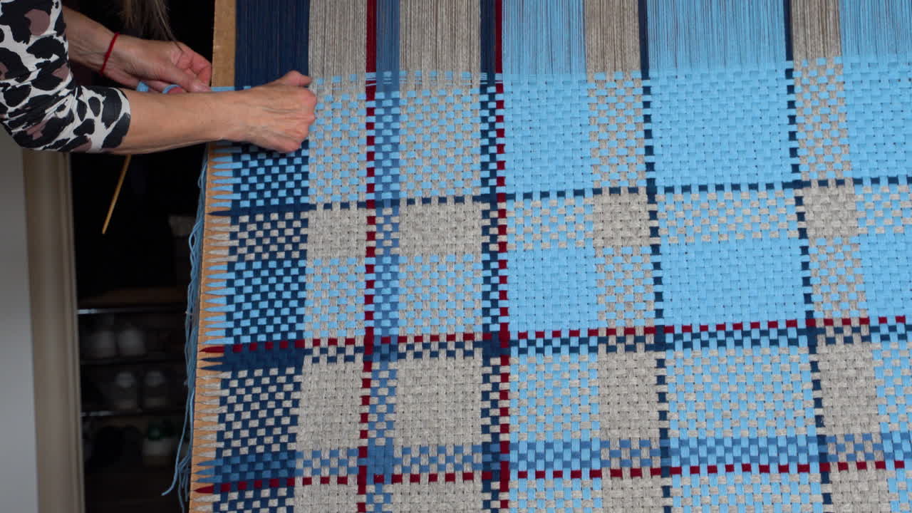 Woman Adjusting Threads on a Blue and Beige Blanket on vertical loom