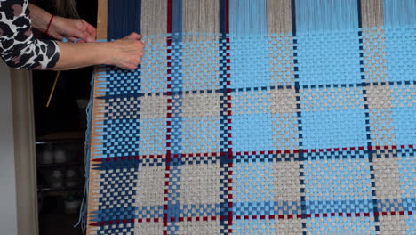 woman adjusting threads on a blue and beige blanket on vertical loom