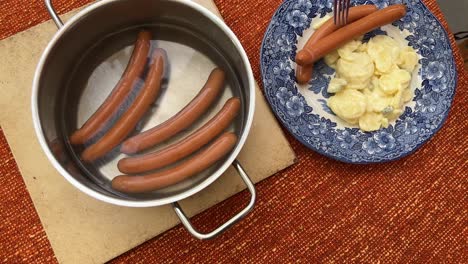 poniendo típica salchicha de bockwurst alemana en un plato con ensalada de patatas recién hecha vista de ángulo alto