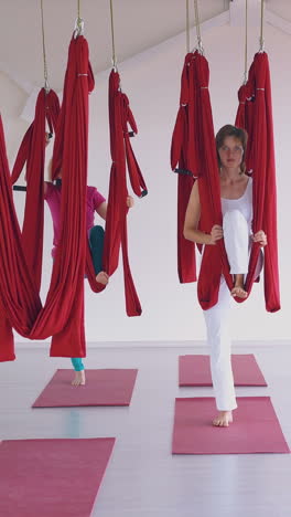 sporty ladies group prepares for oriental fly yoga workout with bright red hammocks in new white gym pilates zone