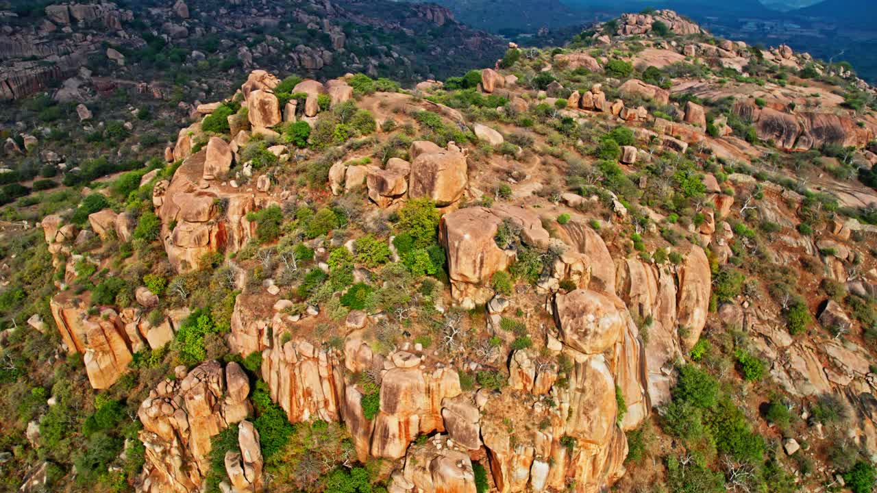 rocky hillscape surrounded by lush greenery with haze and clouds shadows at day time, push in, tilt down, drone shot, 4k.