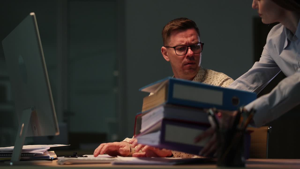 Man Overwhelmed by Excessive Workload and Binders in Late Night Office