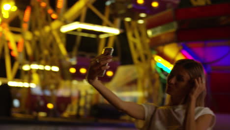 Young-blonde-woman-enjoys-bright-lights-of-carnival-while-taking-a-selfie