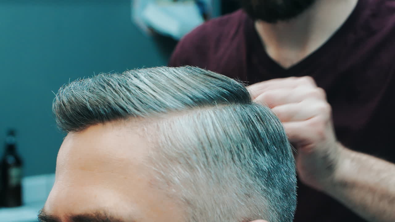 Barbiere che crea un'acconciatura con il pettine. Primo piano delle mani maschili del parrucchiere.