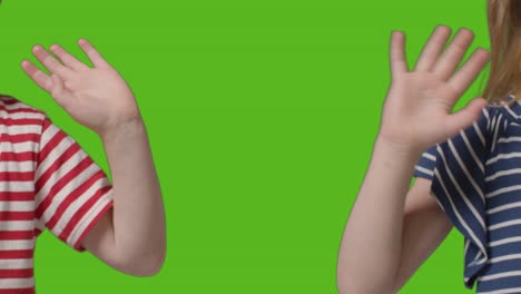 close up of two young children waving to camera against green screen