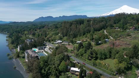orbiting drone view over lush hillside and lakefront buildings near snow-capped villarrica volcano in southern chile