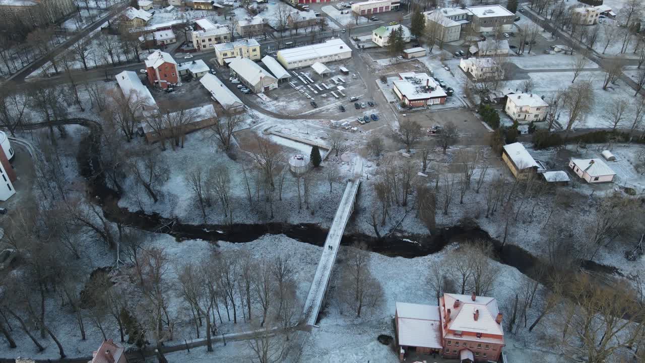 A breathtaking aerial view of Valmiera city, showcasing the winding Gauja River surrounded by snow-covered landscapes and residential areas under a wintry sky.