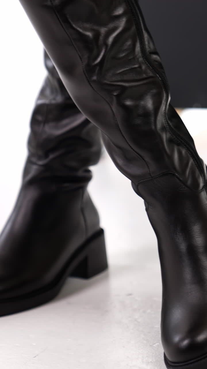 Beautiful elegant stylish female boots presentation. Lady turning and showing fashionable footwear at white floor backdrop. Close up. Vertical video