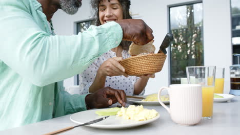 una pareja bi-racial feliz con huevos revueltos para el desayuno y hablando en la cocina, en cámara lenta.