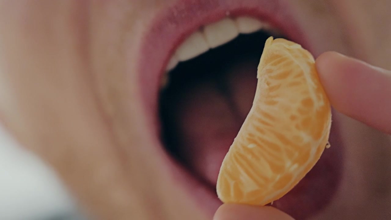 Cámara lenta destaca una mandarina jugosa antes de un bocado, celebrando la nutrición natural.